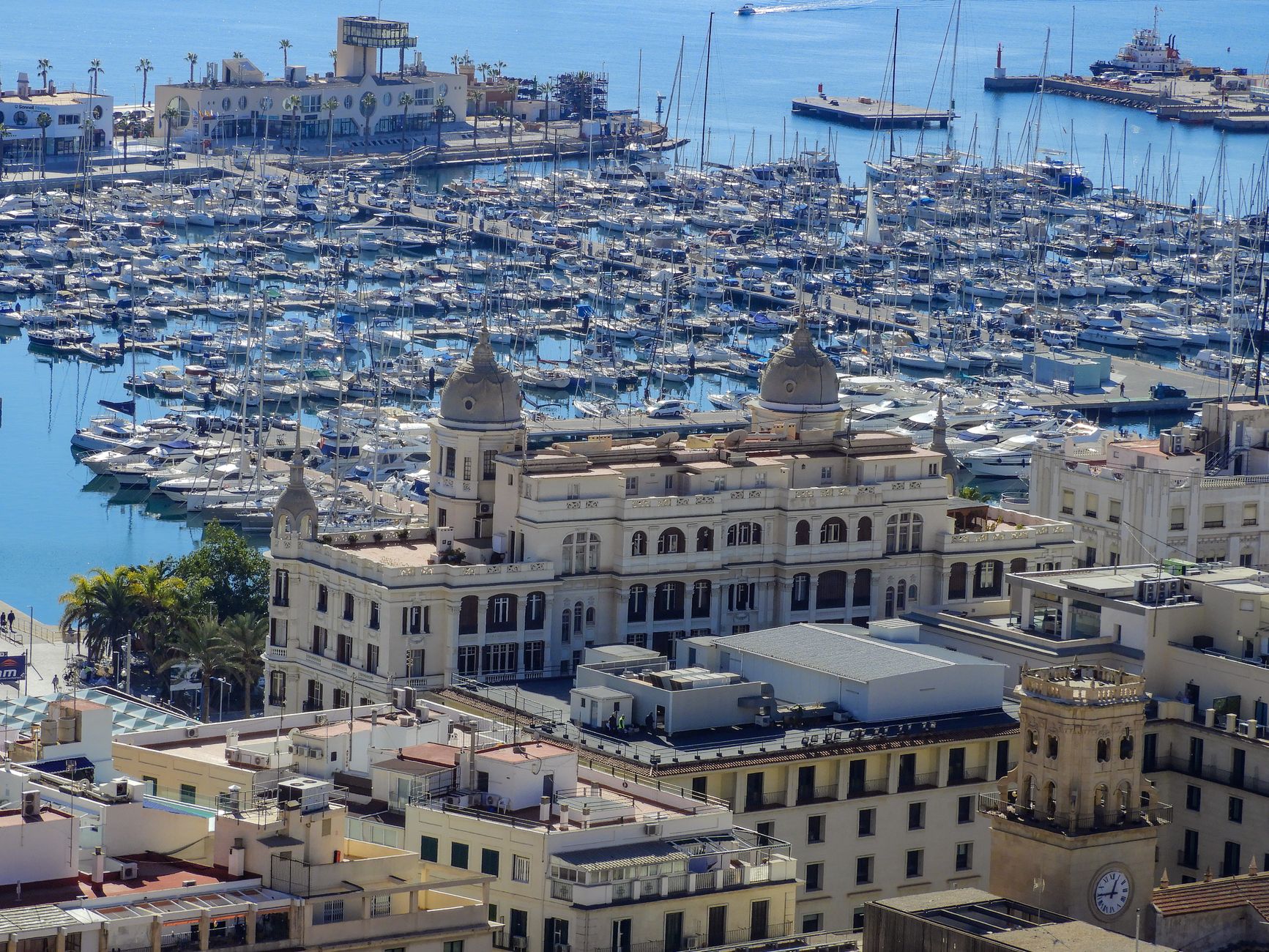 Aerial view of Alicante marina with boats and historic architecture under a clear blue sky.