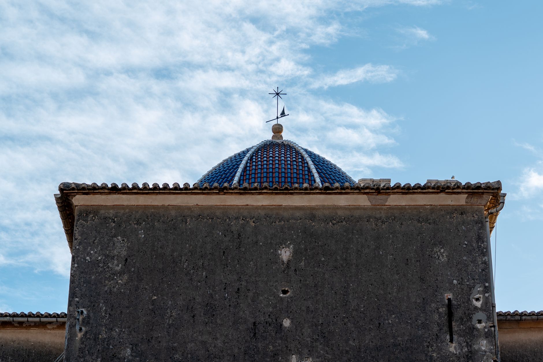 Historic building with a blue tiled dome in Denia, Spain under a partly cloudy sky.