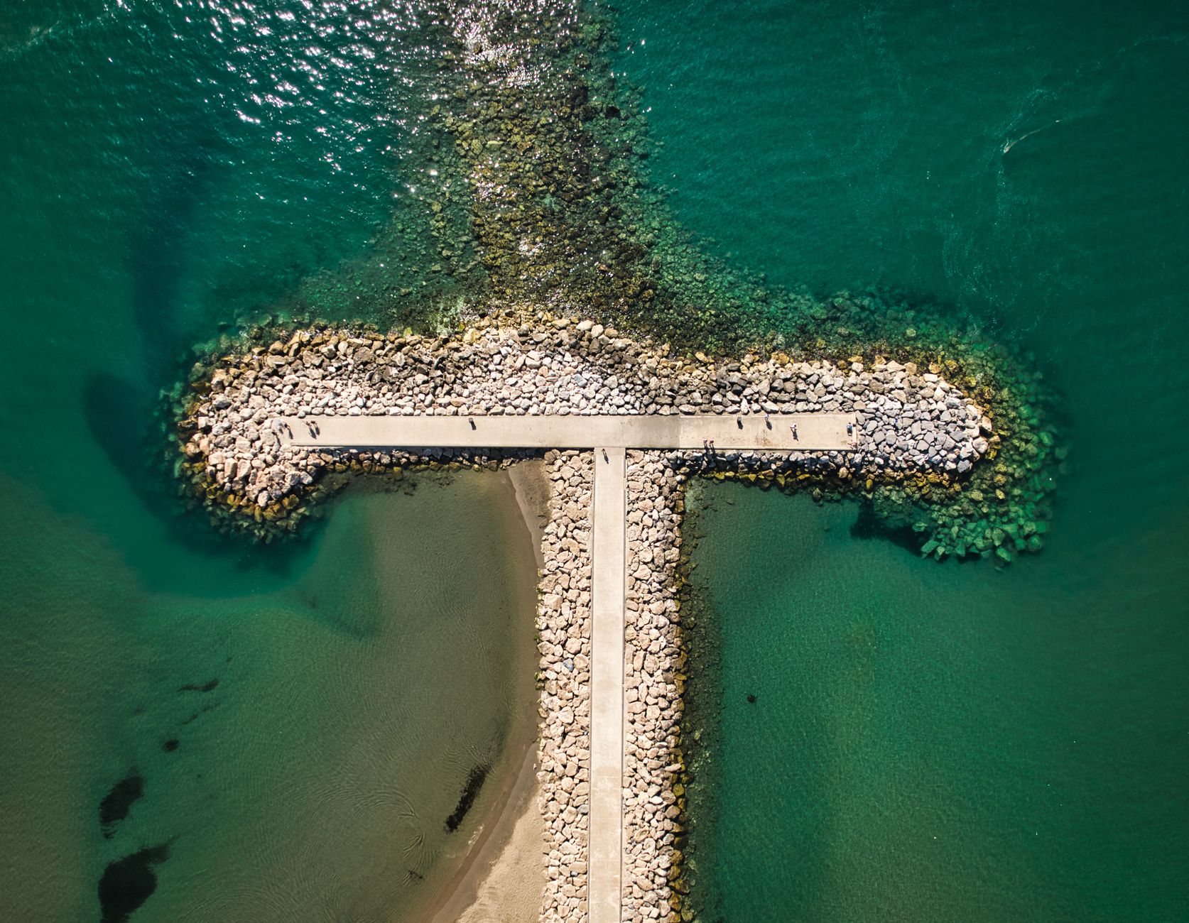 A aerial view of a breakwater in Fuengirola, Spain, surrounded by clear blue waters.