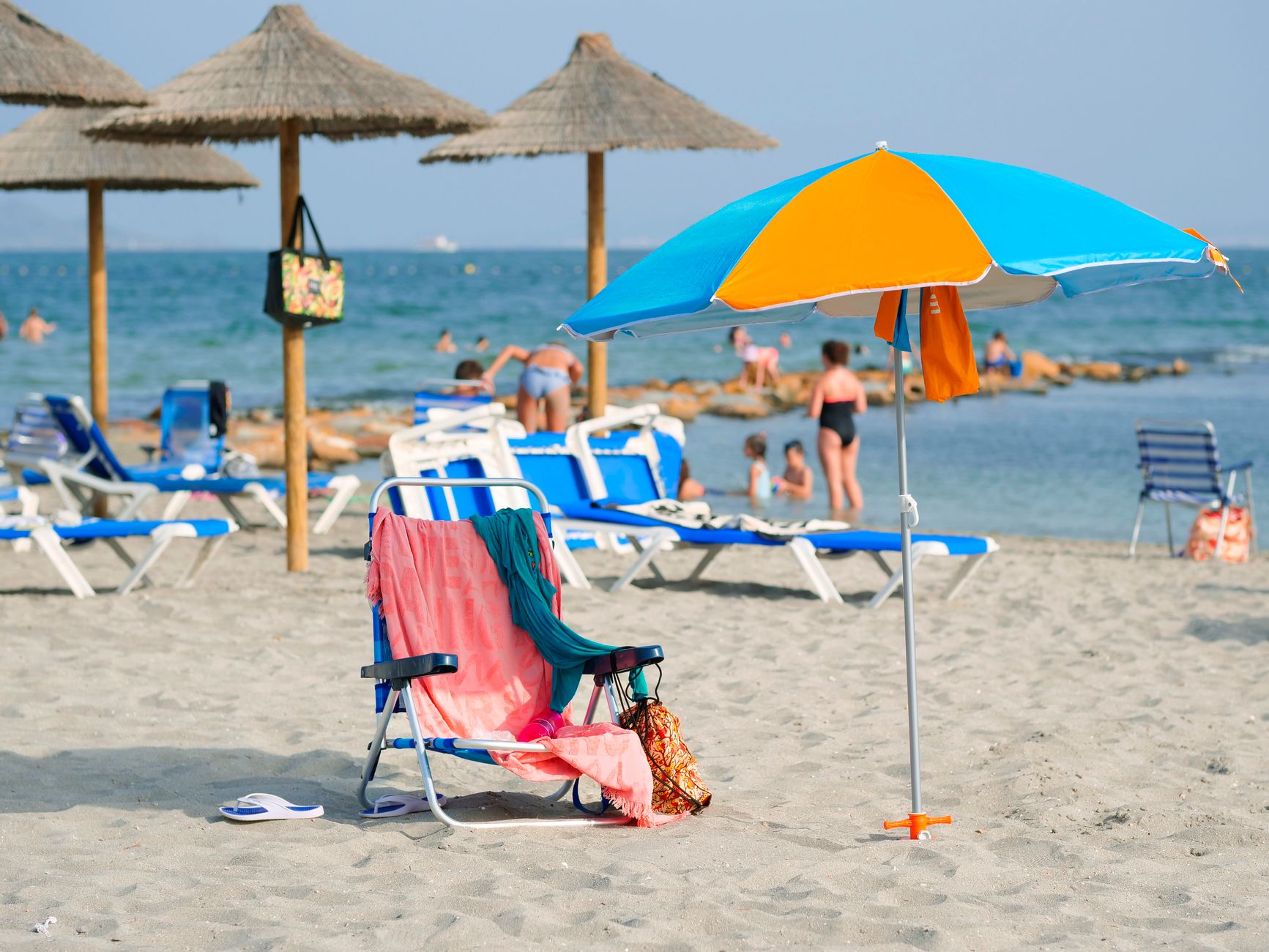 Relaxing beach scene in Los Alcázares, Spain, featuring bright umbrella, loungers, and people enjoying the sun.