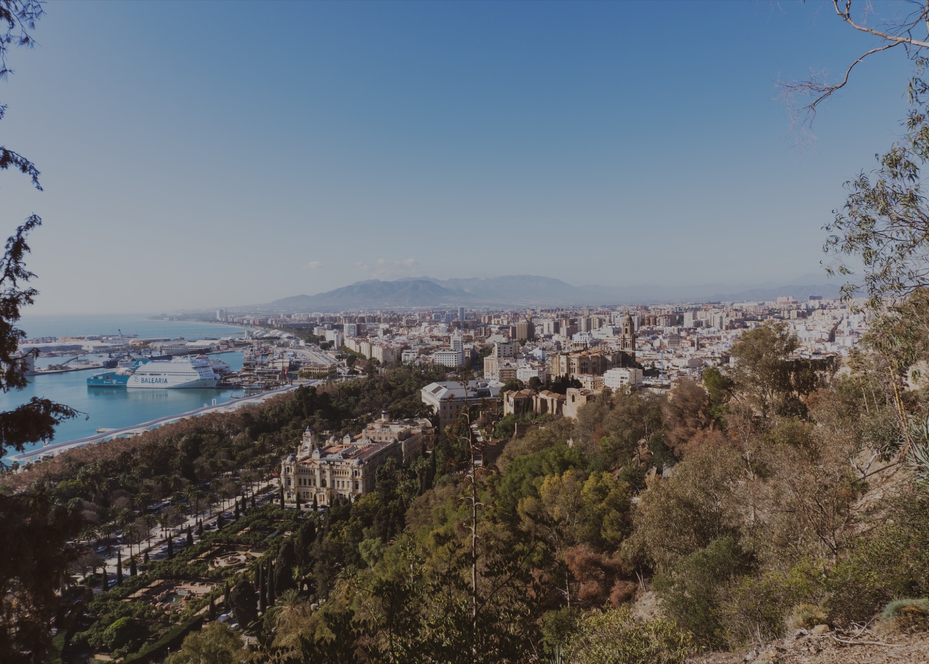 Aerial view of Málaga cityscape with harbor and greenery under a clear blue sky.