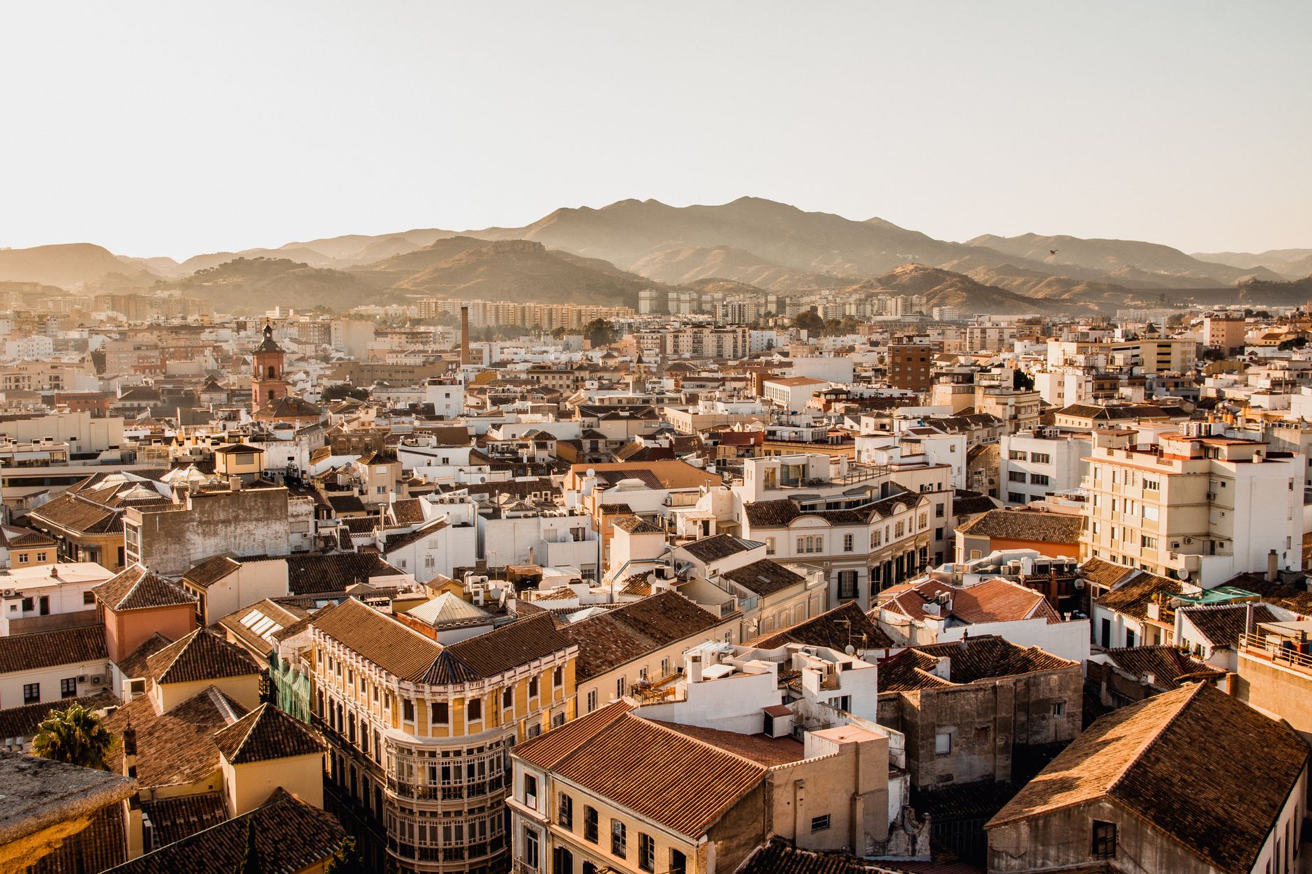 Aerial view of Málaga's cityscape with mountains in the background during sunset.