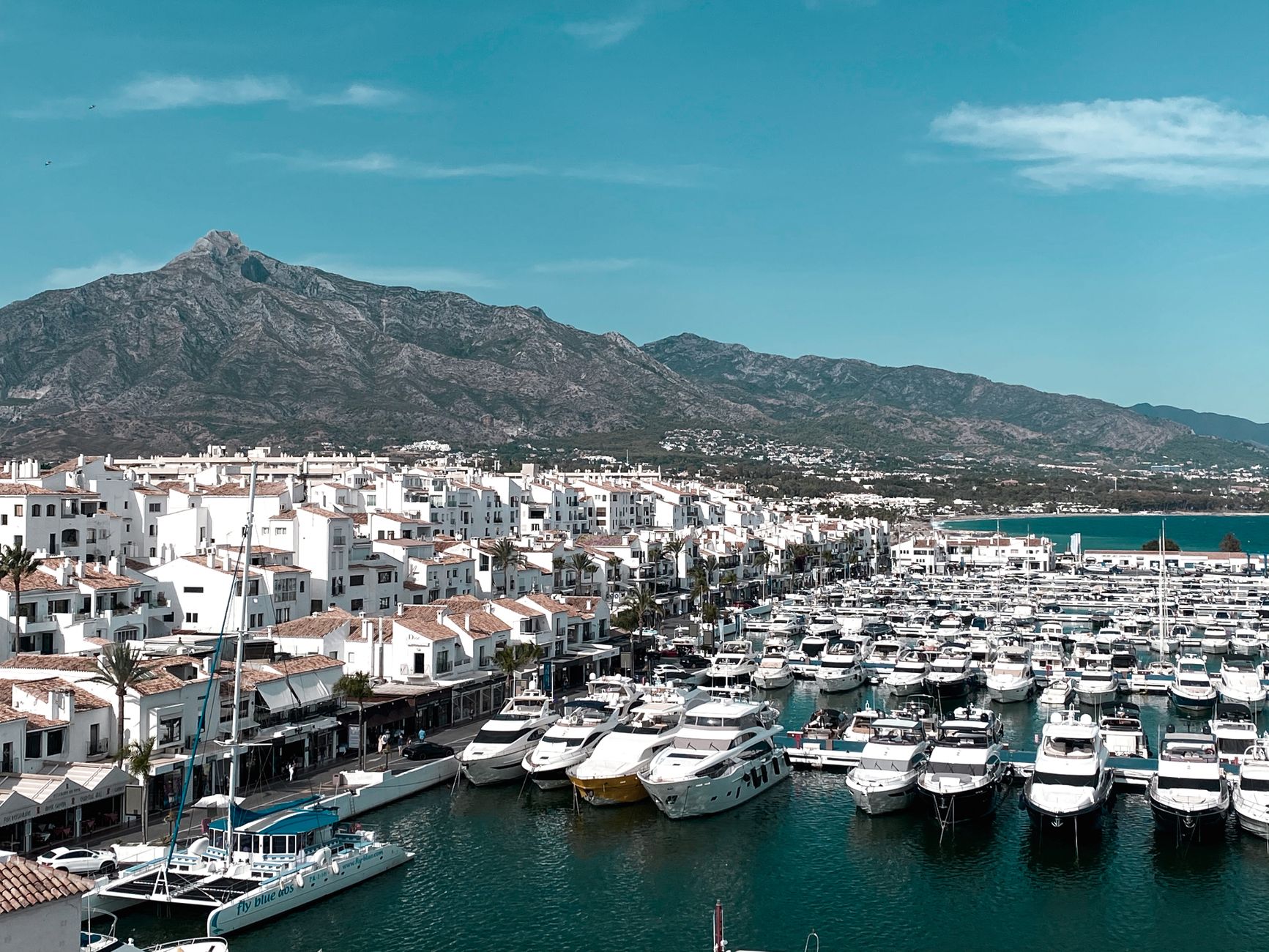 Aerial view of Marbella marina with many yachts and a mountain backdrop.