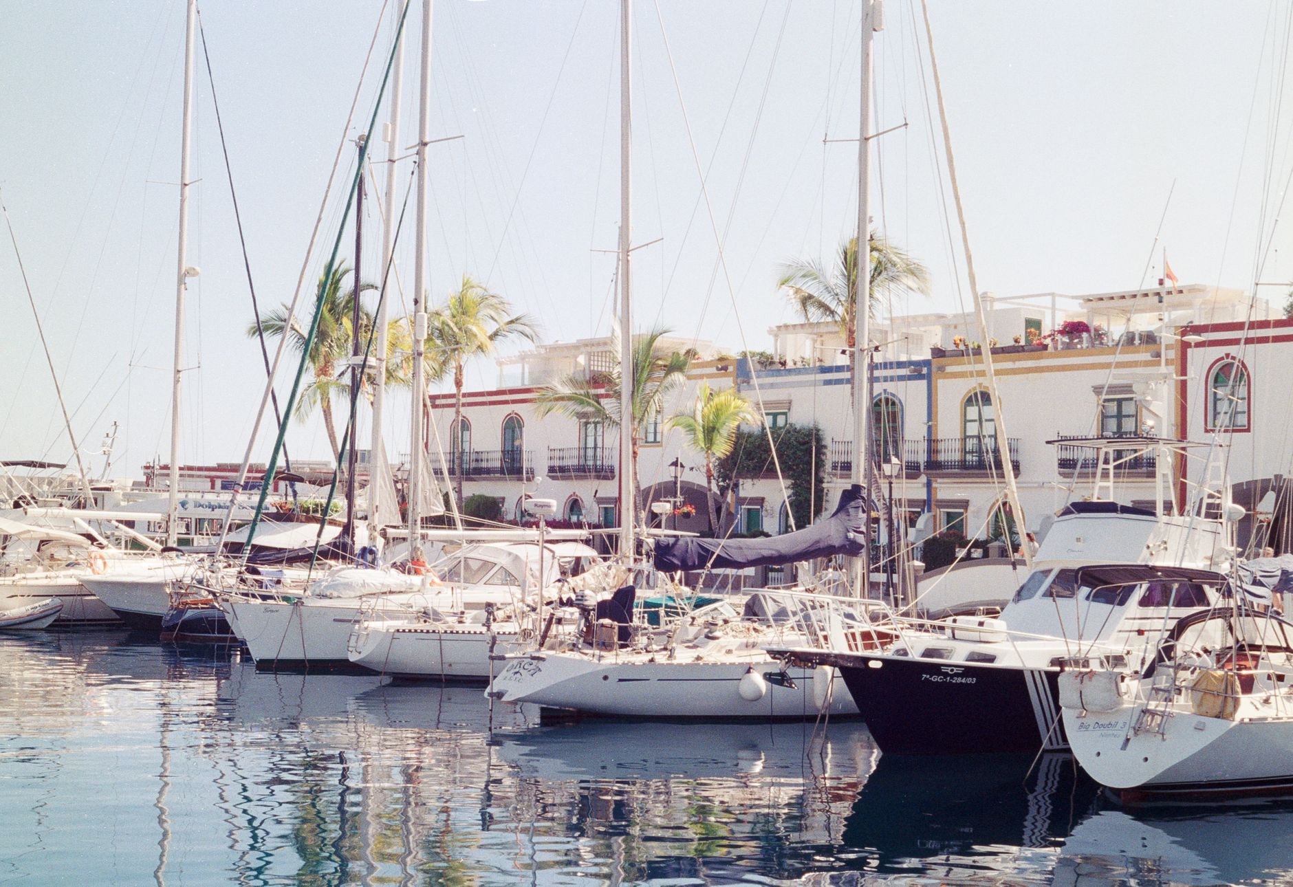 Colorful view of yachts docked at Puerto de Mogán marina in Spain, with palm trees and buildings.
