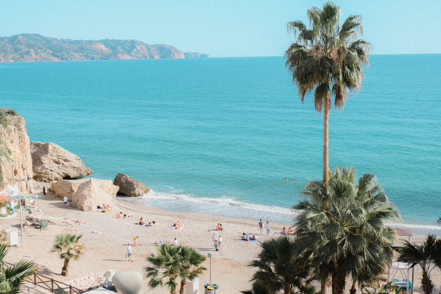 Beach scene in Nerja, Andalusia, Spain featuring palm trees and clear blue sea.