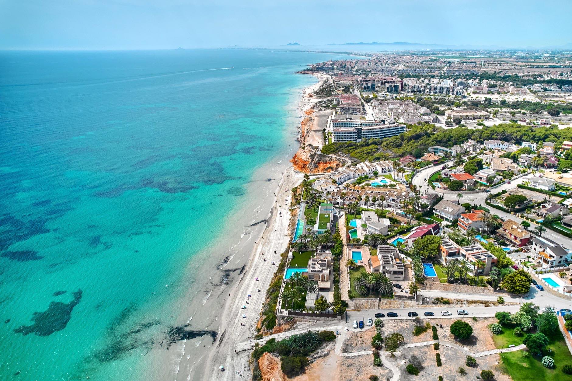 Aerial shot Dehesa de Campoamor, village in Orihuela Costa. Residential area with houses, surrounded by greenery, apartment buildings near coastline, sandy beach, Mediterranean Sea view. Spain