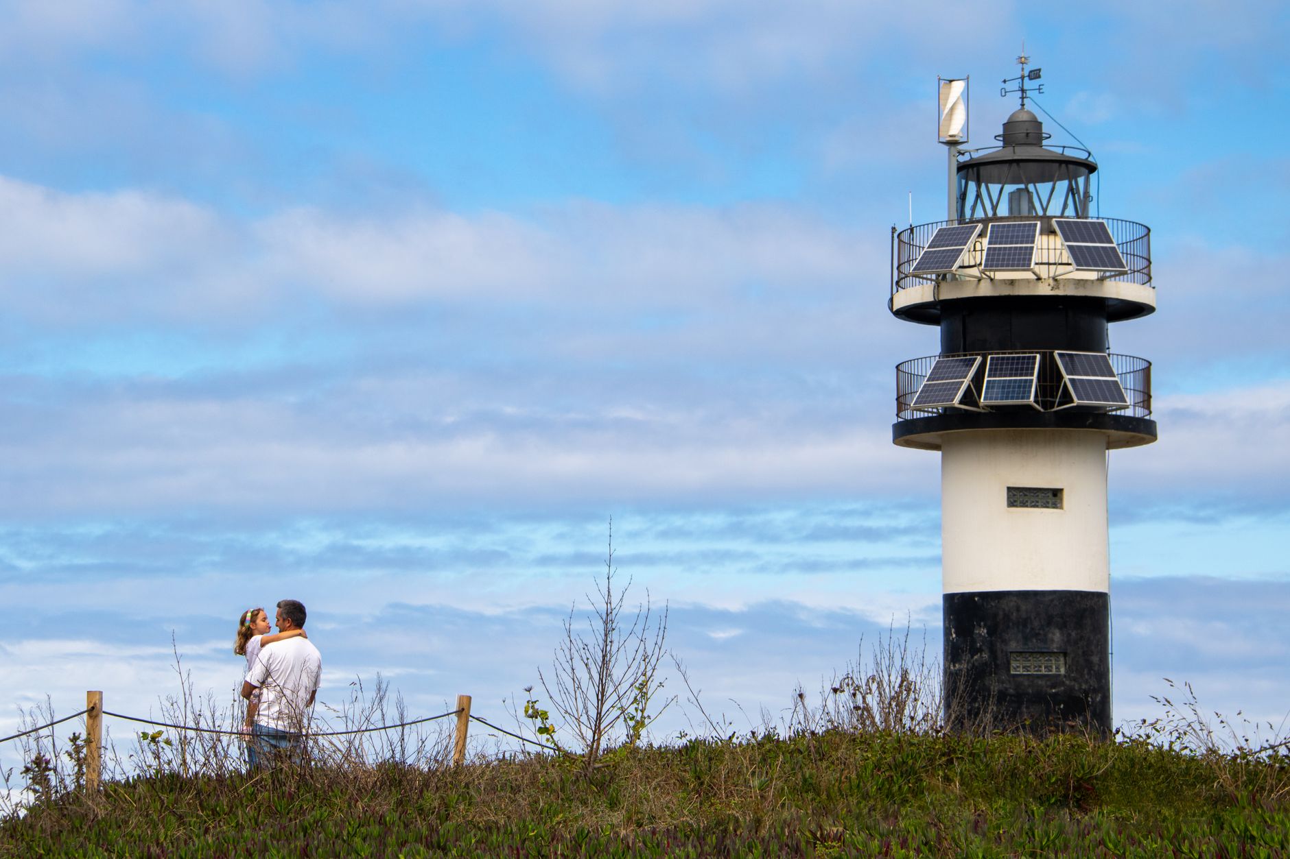 A heartwarming scene of a father and daughter by Ribadeo lighthouse under a blue sky.