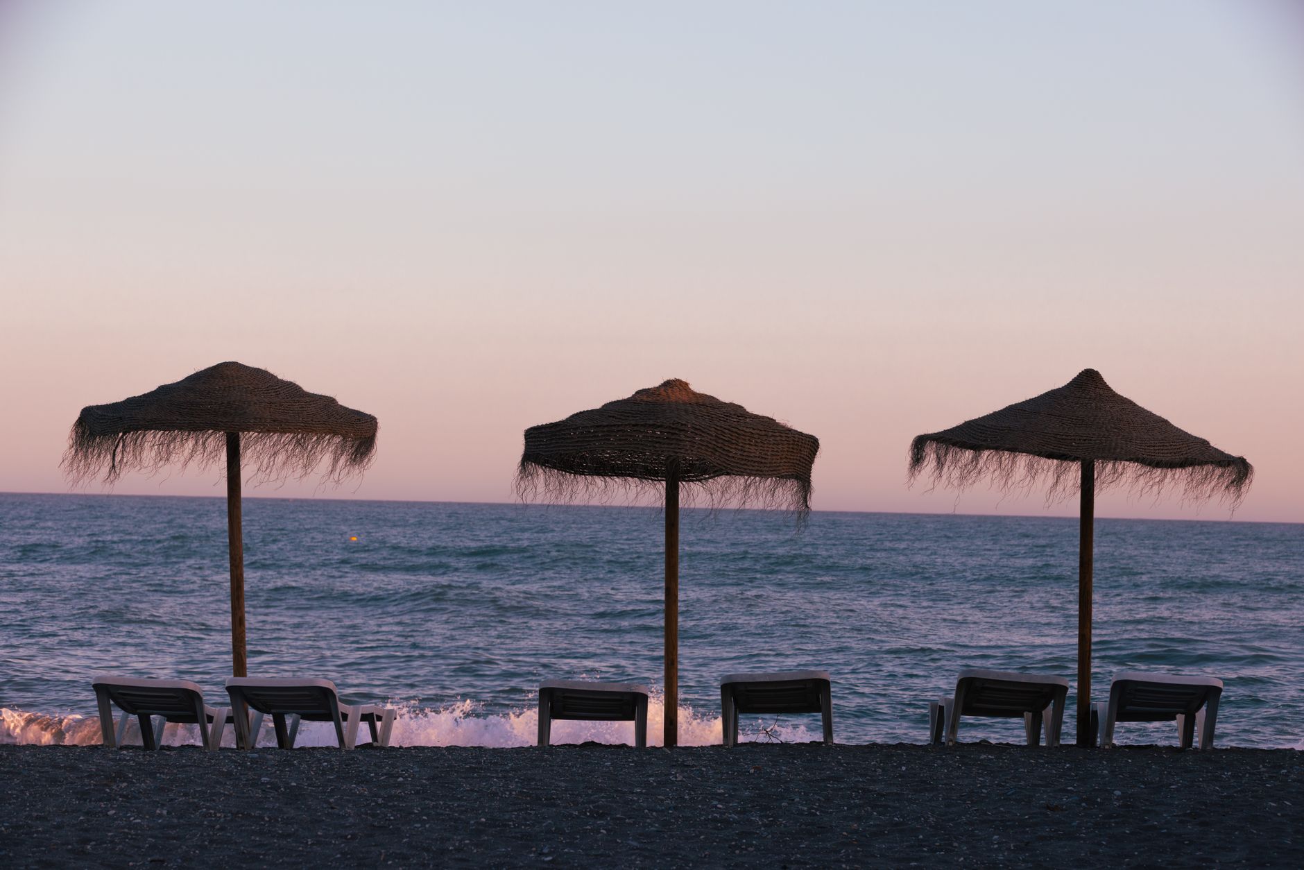 Peaceful Torrox Costa beach scene with chairs, umbrellas, and pastel sky.