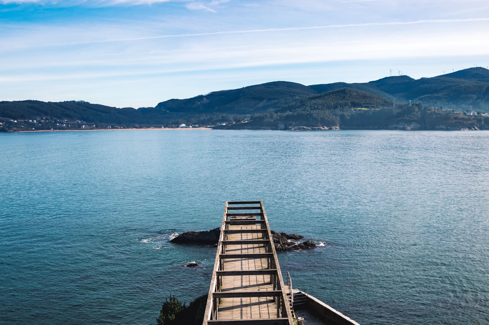 A pier extends into the waters of Viveiro Bay with hills in the background. Perfect for travel and nature imagery.